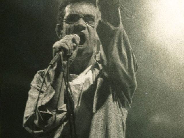 Fotografia em preto e branco de Renato Russo cantando ao microfone.